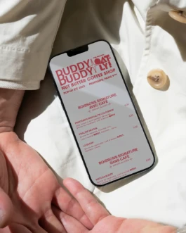Smartphone displaying the digital menu of the Buddy Buddy x Oatly Nut Butter Coffee Shop pop-up at Printemps, Paris, with signature drinks listed.