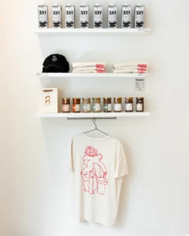 White t-shirt with a red line illustration, designed for the Buddy Buddy x Oatly pop-up event at Printemps Paris, displayed on a hanger among branded products.