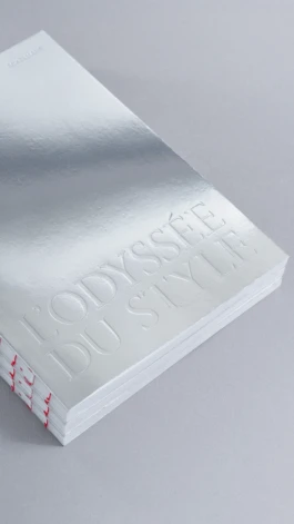 Close-up of L’Odyssée du Style book cover by Astrid Eckelmans, with mirror chrome finish, embossed typography, and red thread exposed binding. Editorial design and art direction by Hank Studio.